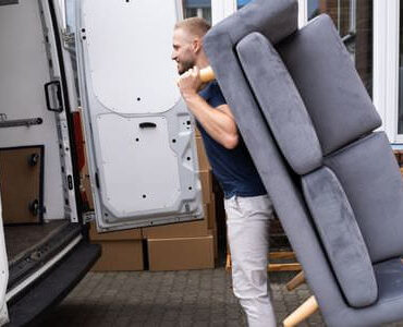 Möbellift Bad Homburg: Helfer tragen ein graues Sofa aus einem Transporter